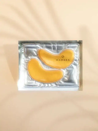 Gold hydrogel eye mask patches in foil packaging on a beige background