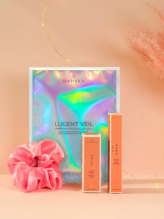 Hadaka Lucent Veil skincare product set with HALO Hair Oil, AURA Hair perfume and pink scrunchie on a peach background