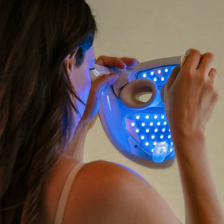 Person using a handheld blue LED light therapy mask on a neutral background
