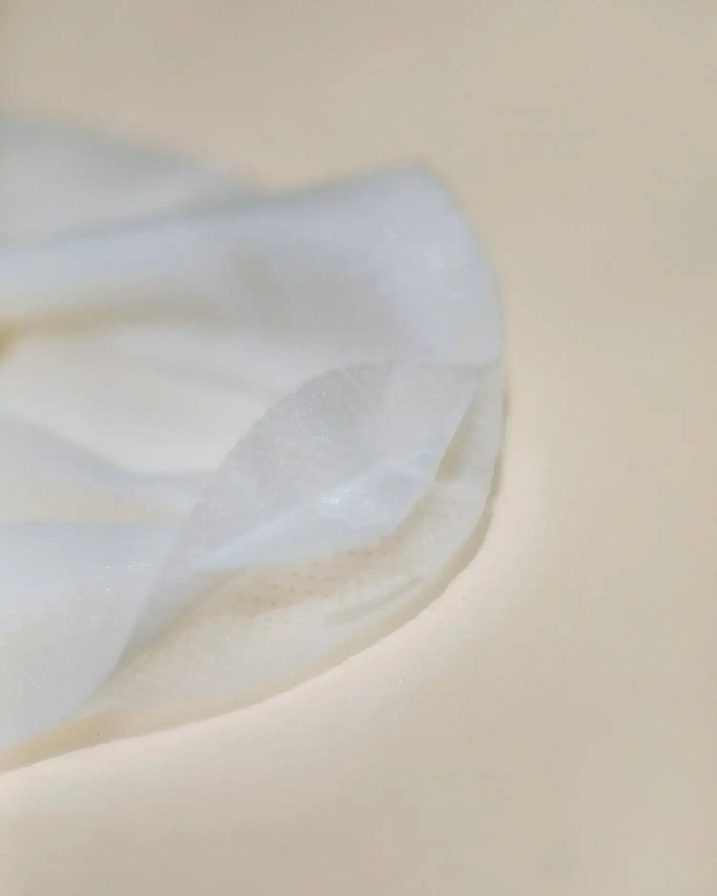 Close-up of thin hydrating face mask layers on a neutral background