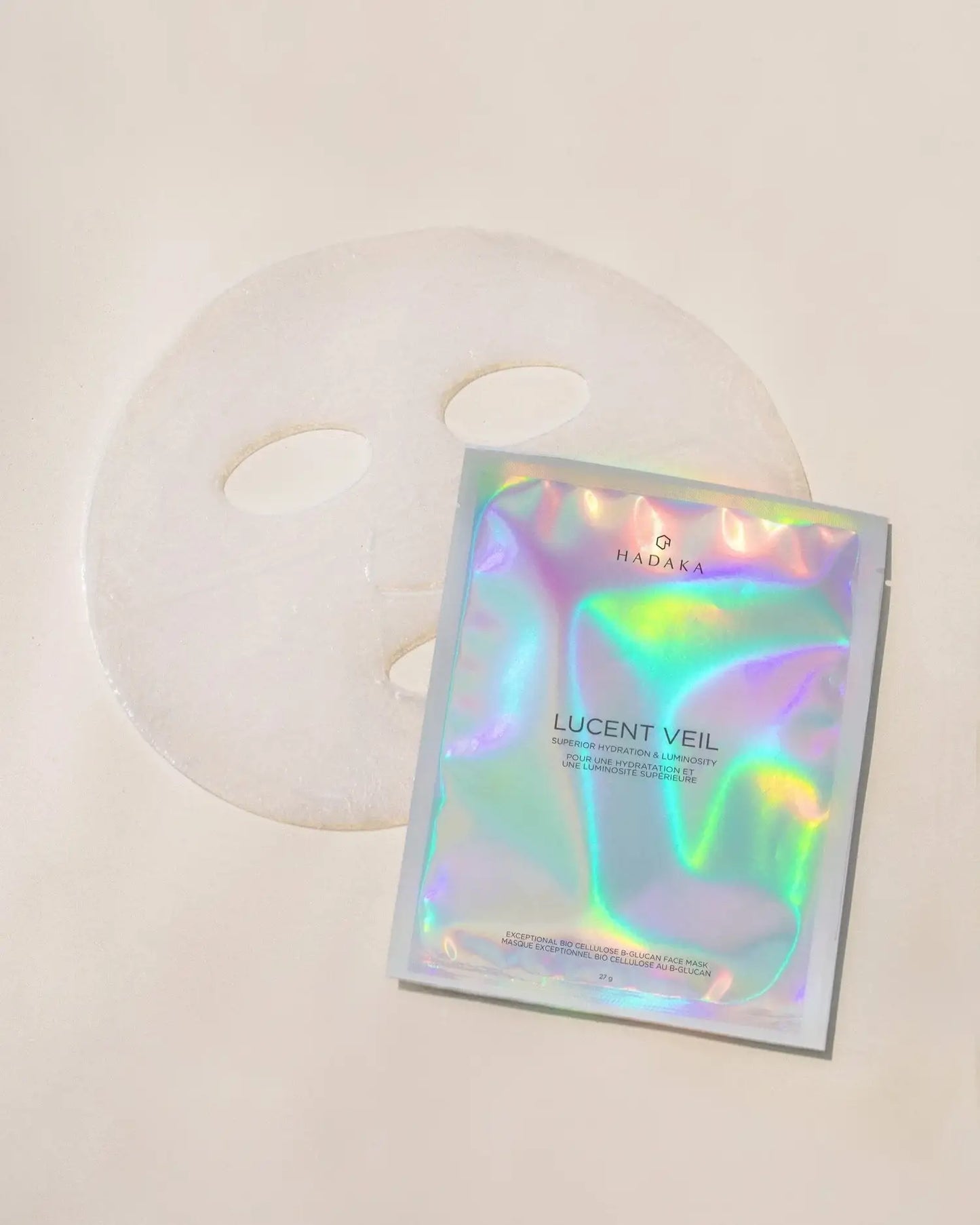 Bio-cellulose face mask sheet with iridescent Lucent Veil mask pouch on beige background