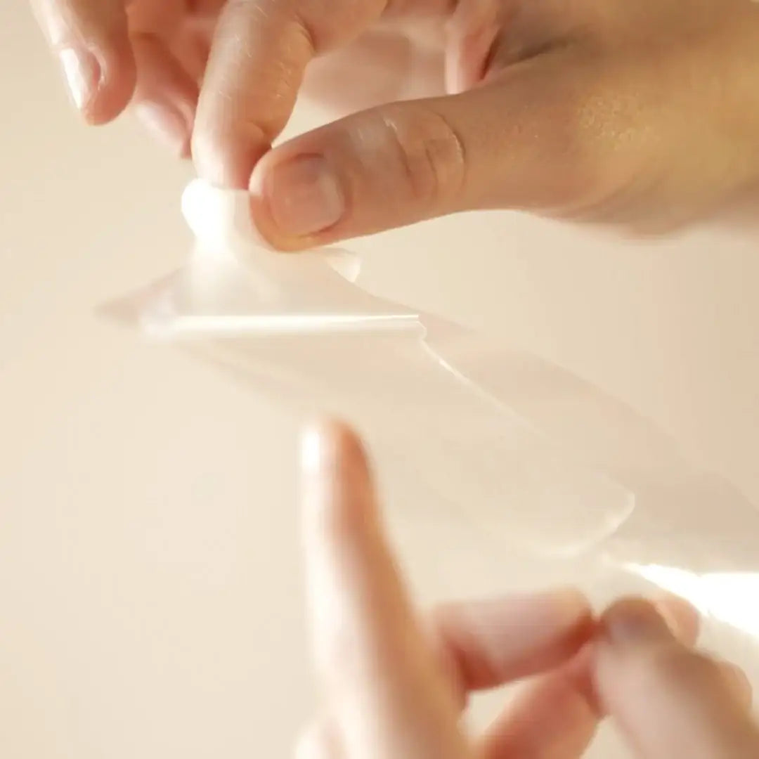 Hand peeling a hydrating eye mask patch, close-up clean skincare product