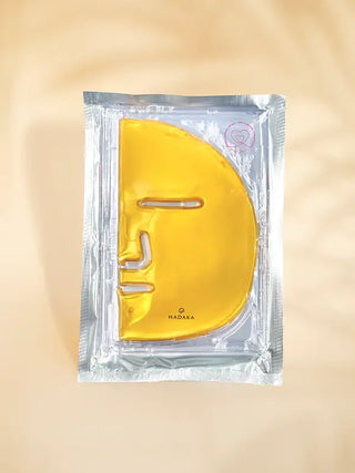 Gold hydrating facial mask in clear packaging for skincare on beige background