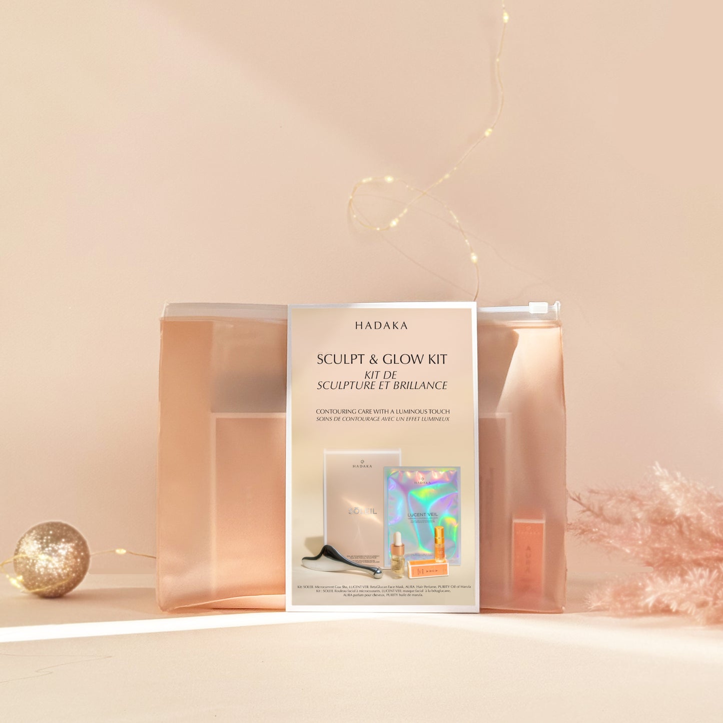 Hadaka Sculpt & Glow Kit packaging with Microcurrent Gua Sha, Beta-Glucan Mask, Marula Oil, and Hair Perfume on a light pink background