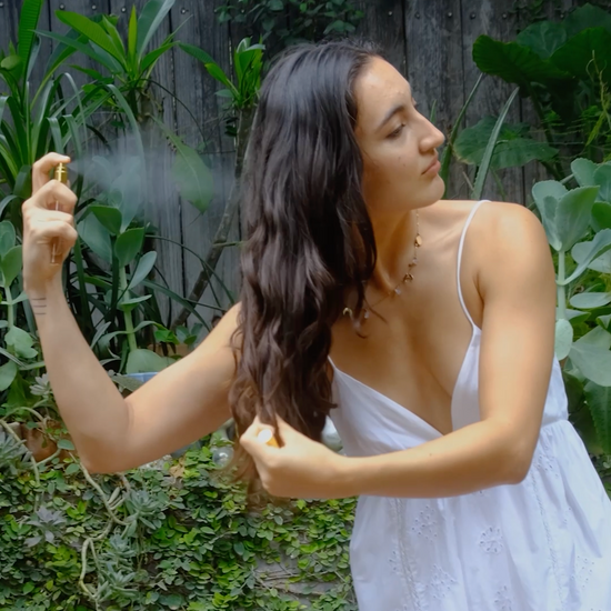 a girl in a natural garden ambiance spraying hair perfume on her hair