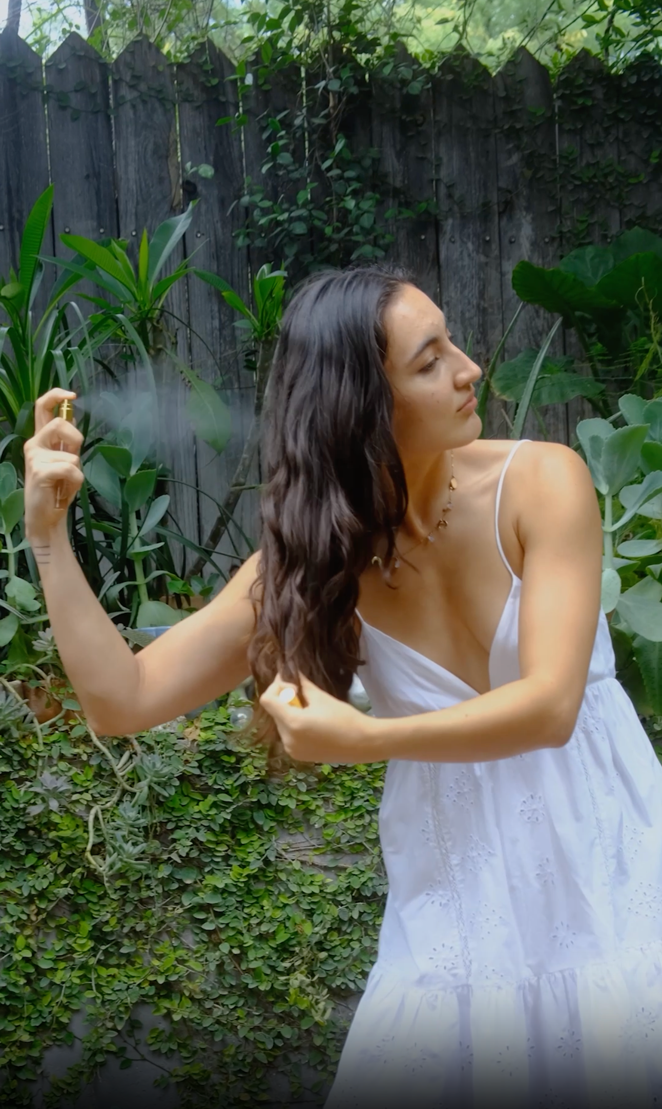 a girl in a natural garden ambiance spraying hair perfume on her hair