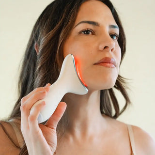Woman using red light therapy face massage device on her face with a neutral background