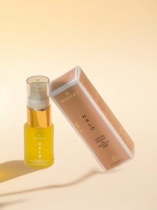 Hadaka Halo hair oil with marula and broccoli seed in glass bottle and box on neutral background