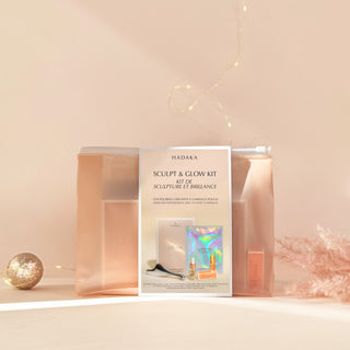 Hadaka Sculpt & Glow Kit packaging with Microcurrent Gua Sha, Beta-Glucan Mask, Marula Oil, and Hair Perfume on a light pink background